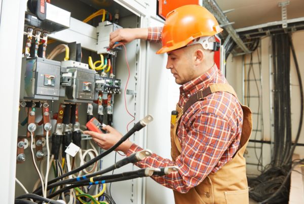 electrician with hardhat and overalls using clamp tester